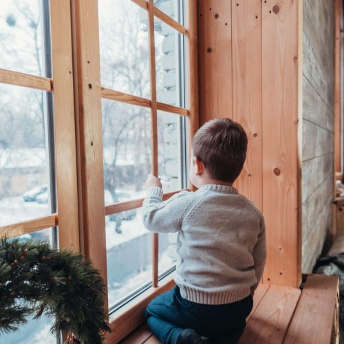 little boy looking out the window holding his hand over the glass, back view